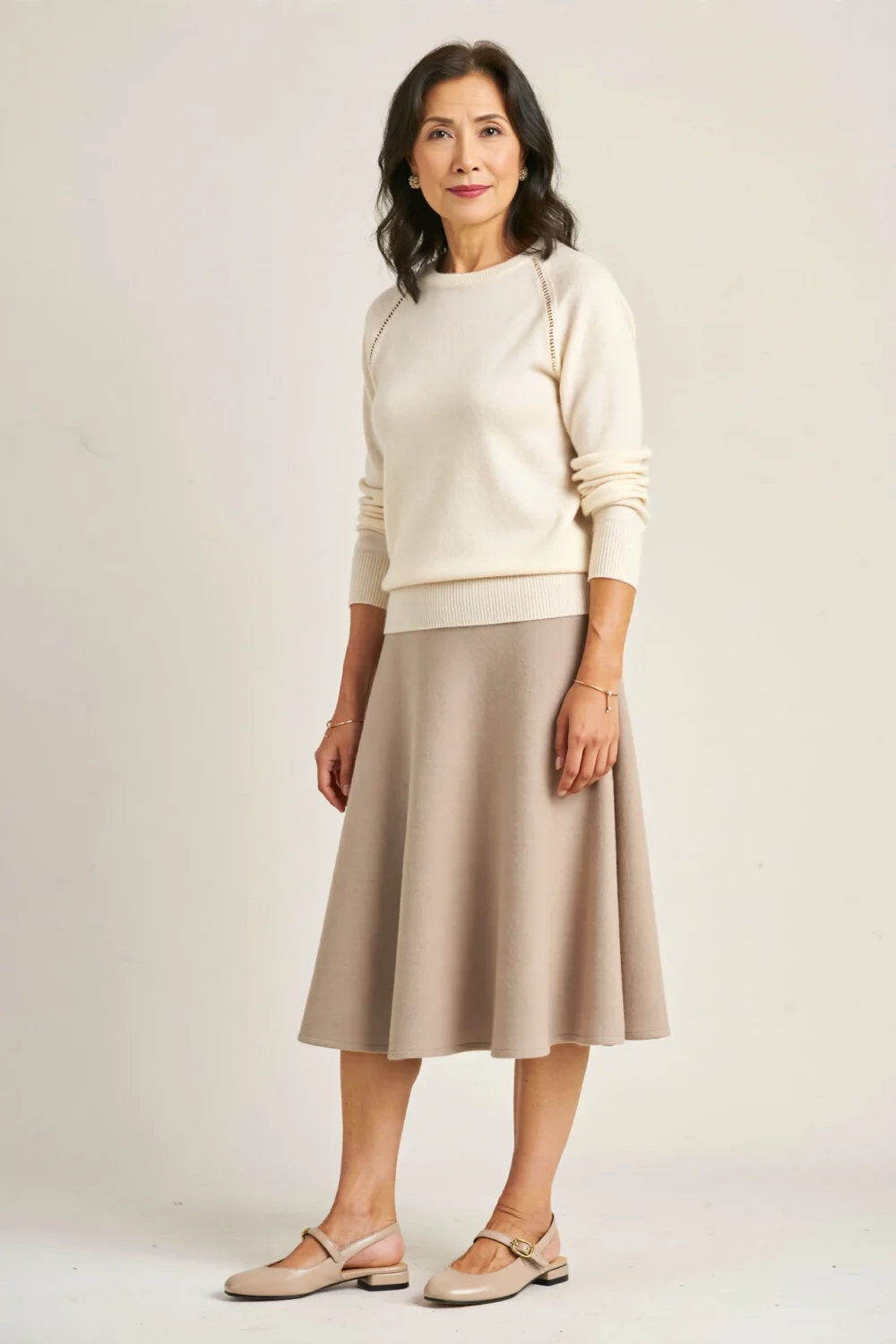 Woman in a cream fine-gauge sweater, A-line midi skirt and slingback flats, styled for a polished 60-year reunion look.