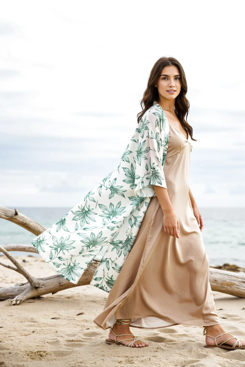 Woman on a beach in an airy floral kimono over a silk slip dress, a floaty bohemian wedding guest look with lightweight coverage.