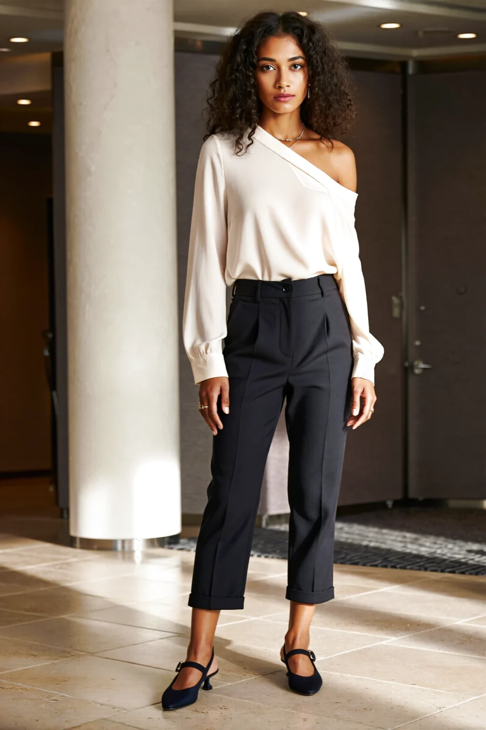 Woman in an off-white asymmetric blouse, tailored black culottes and slingback heels, confident business casual for a career fair.