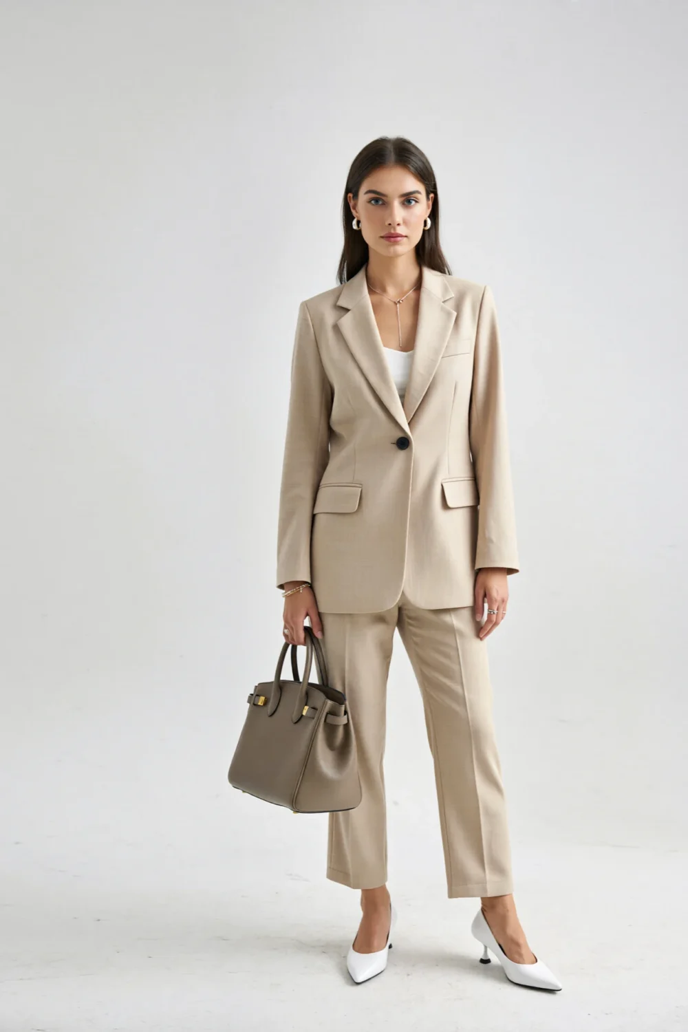 Woman in beige blazer and trousers with white pumps, structured taupe bag and clean-lined jewelry for a crisp minimalist look