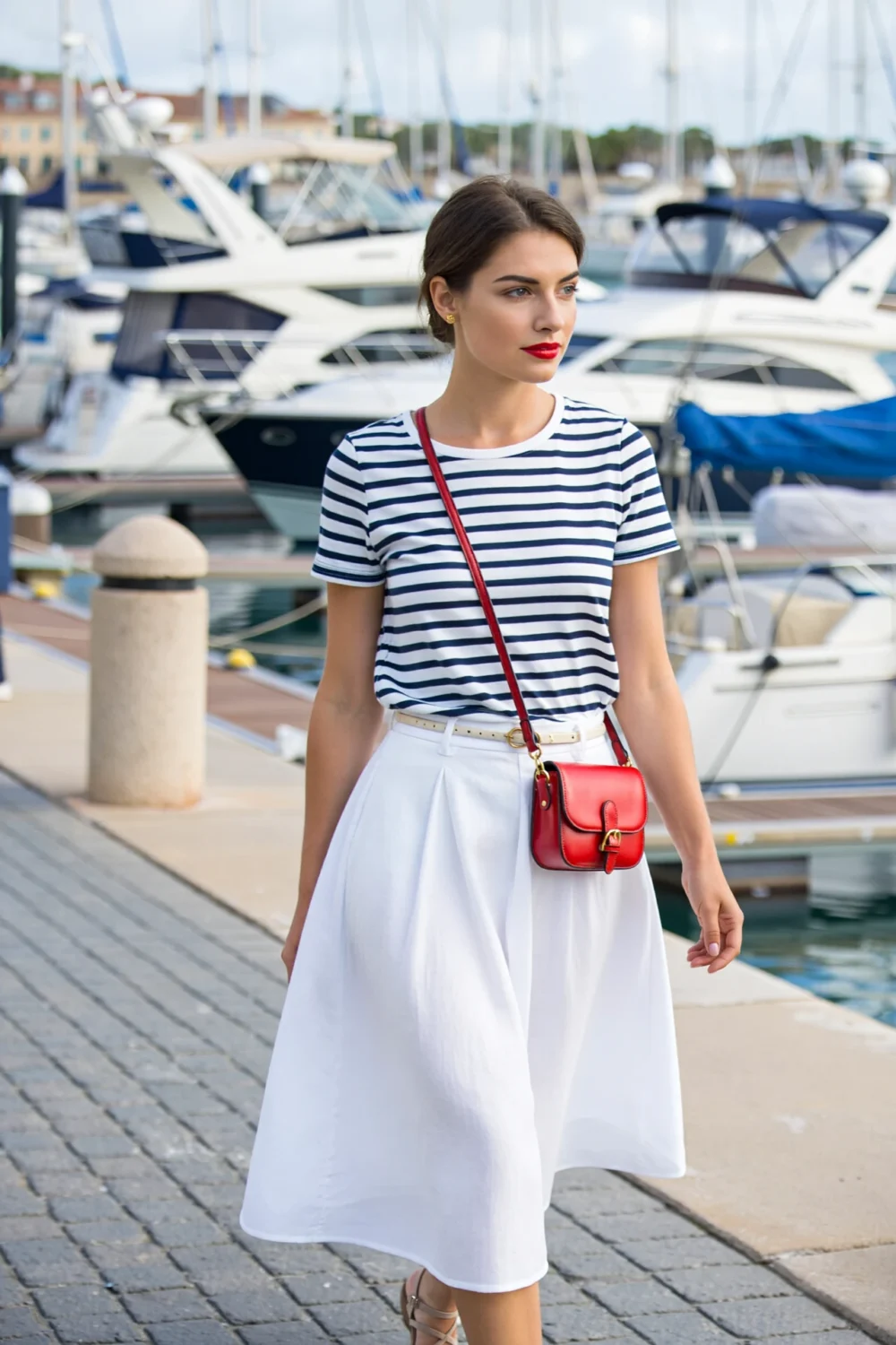 Woman in Breton stripe tee, white A-line maxi skirt, red lip and crossbody at marina, chic nautical editorial style
