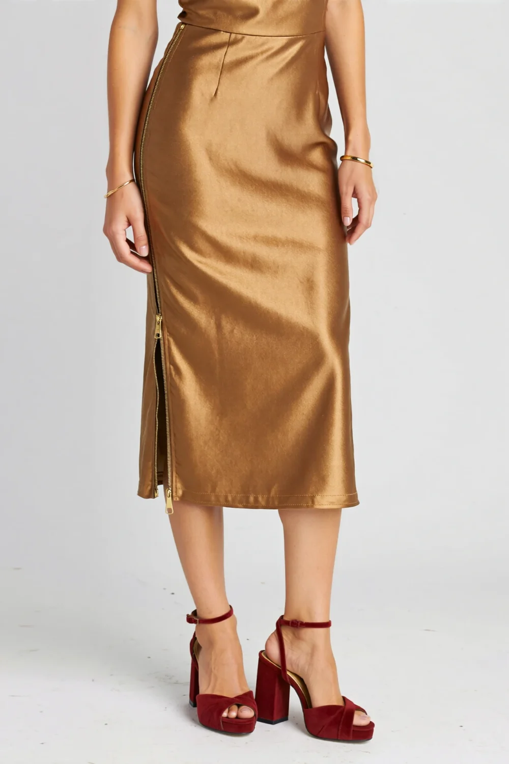 Bronze-toned gold midi sheath dress styled with ruby suede ankle-strap heels, creating a rich, regal, textured outfit contrast