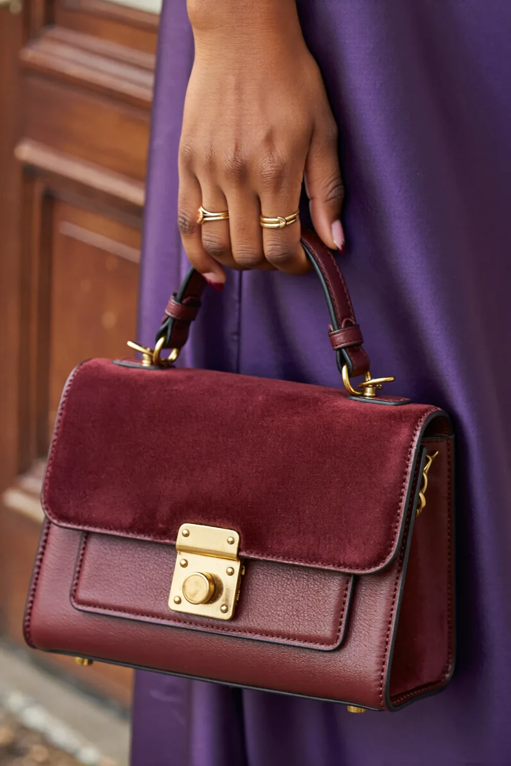 Structured burgundy oxblood purse with gold hardware held against a purple dress, creating a luxe tonal look for cooler seasons