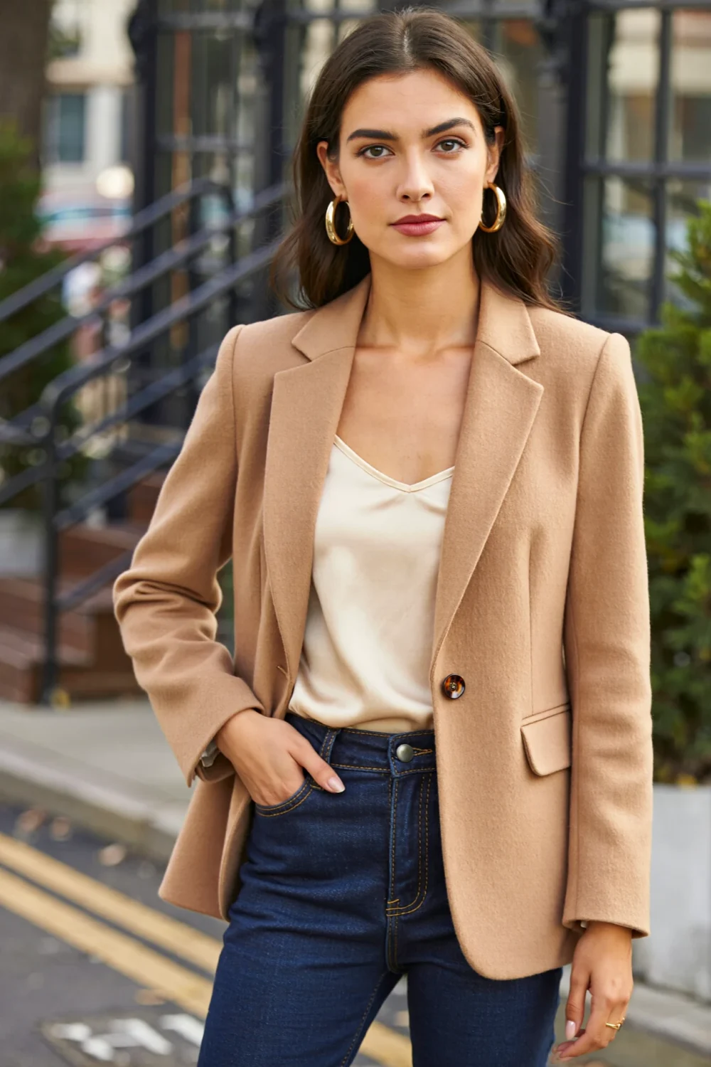 Woman in camel blazer and cream cami with dark straight-leg denim and gold hoops, creating a polished, easy chic outfit.