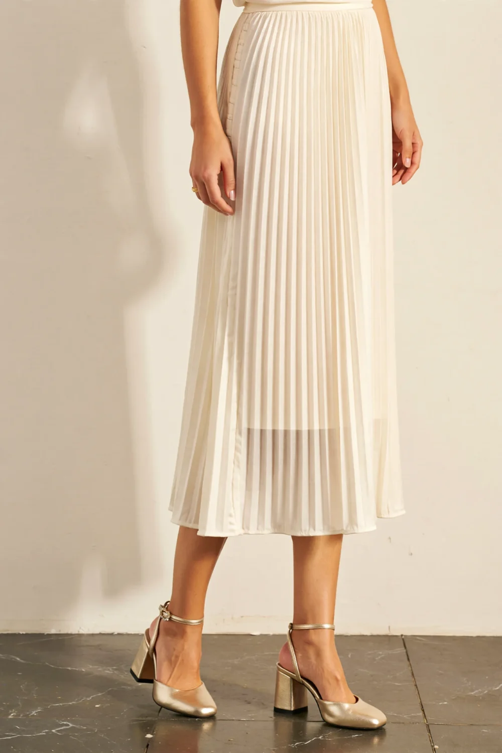 Ivory pleated midi skirt styled with champagne block heels, creating a subtle luxury look with wearable metallic shimmer for events