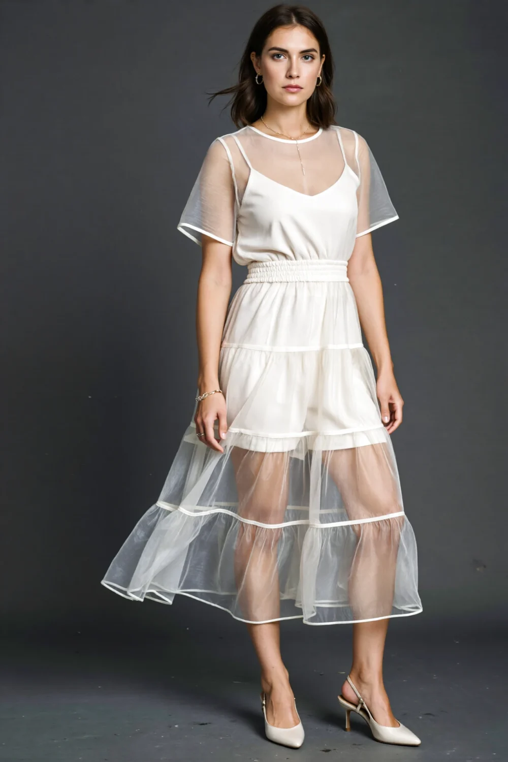 Model wearing ivory mini with chiffon overskirt layered in floaty tiers over a fitted top and elastic waist, sheer sleeves, heels