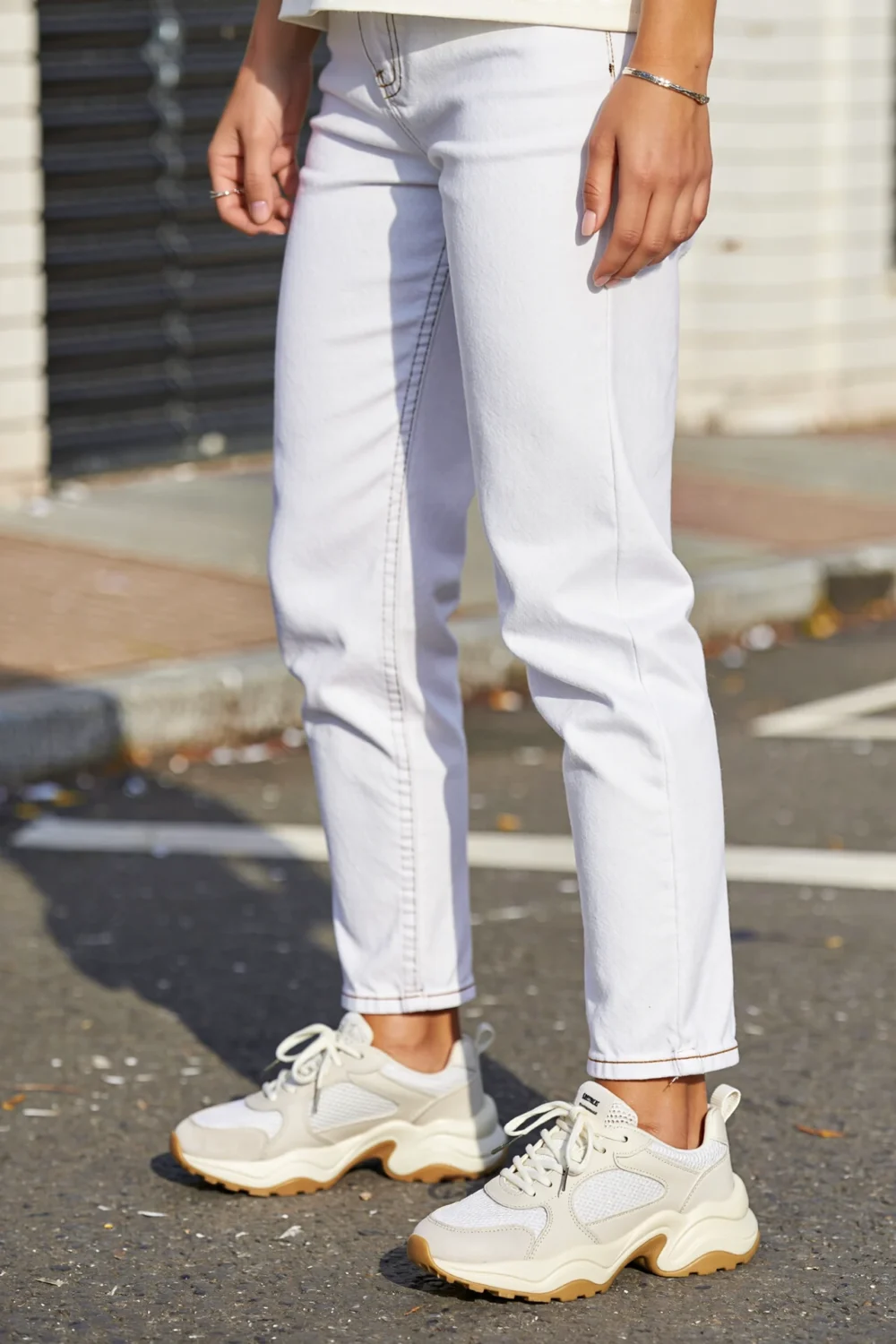 Chunky white trainers with white denim, showing a sporty monochrome street style look with relaxed fit and textured mesh overlays