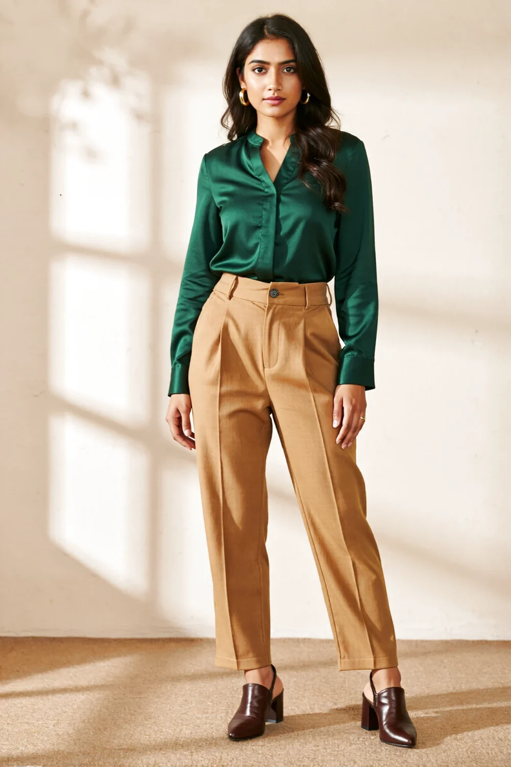 Woman wearing a dark green blouse with caramel khaki trousers, styled with gold hoops and block heels for an autumn-ready look.