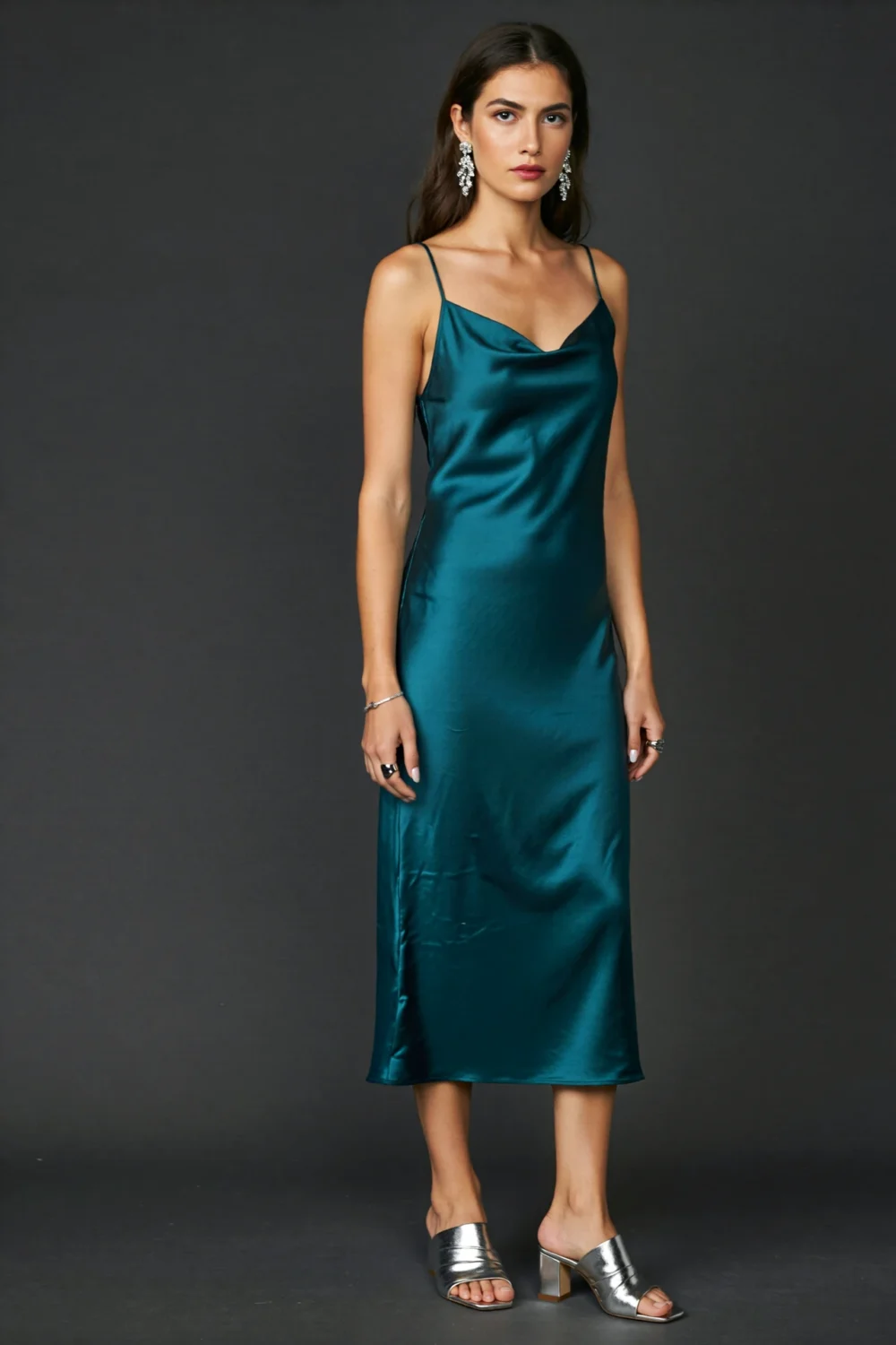 Model in dark teal slip dress with silver mules and statement earrings, creating a sleek, minimalist editorial evening look