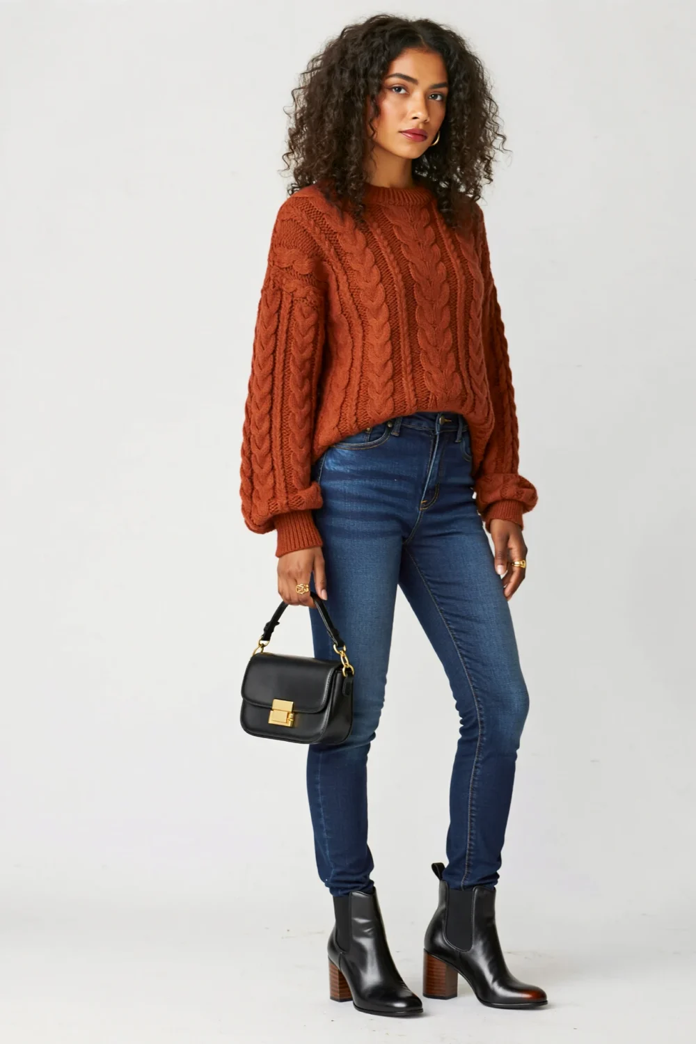 Model in dark-wash jeans, rust cable knit sweater, and heeled black Chelsea boots, styled for a chic autumn Halloween look