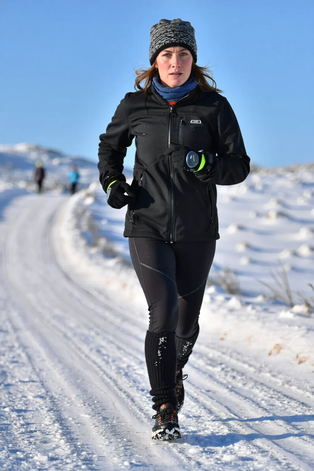 Woman running in Deep Freeze layers: beanie, gaiter, windproof jacket, tights, gaiters and waterproof shoes