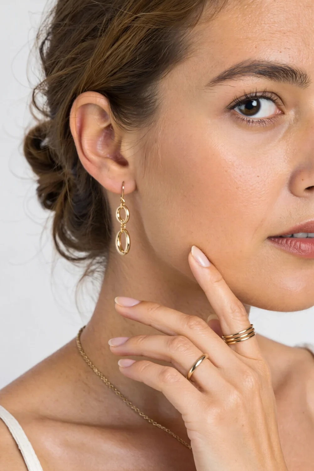 Close-up of woman wearing a collarbone-skimming gold chain, gold drop earrings and stacked gold rings for modern subtle sparkle