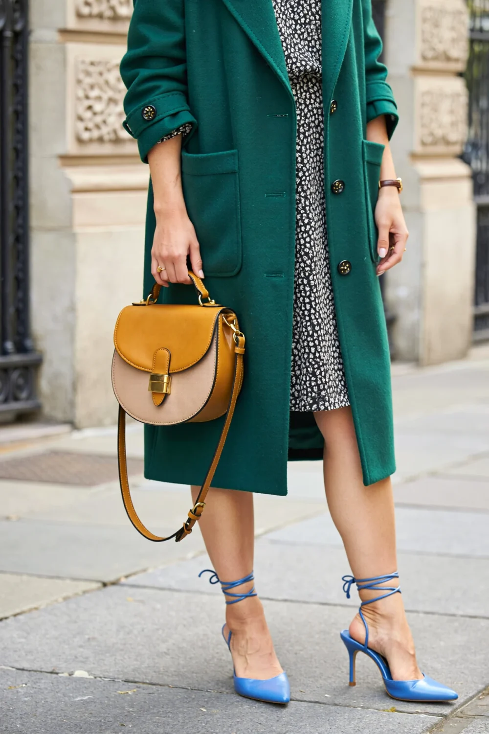 Emerald green coat over a black-and-white microprint dress, paired with periwinkle lace-up stilettos and a mustard-camel half-moon bag