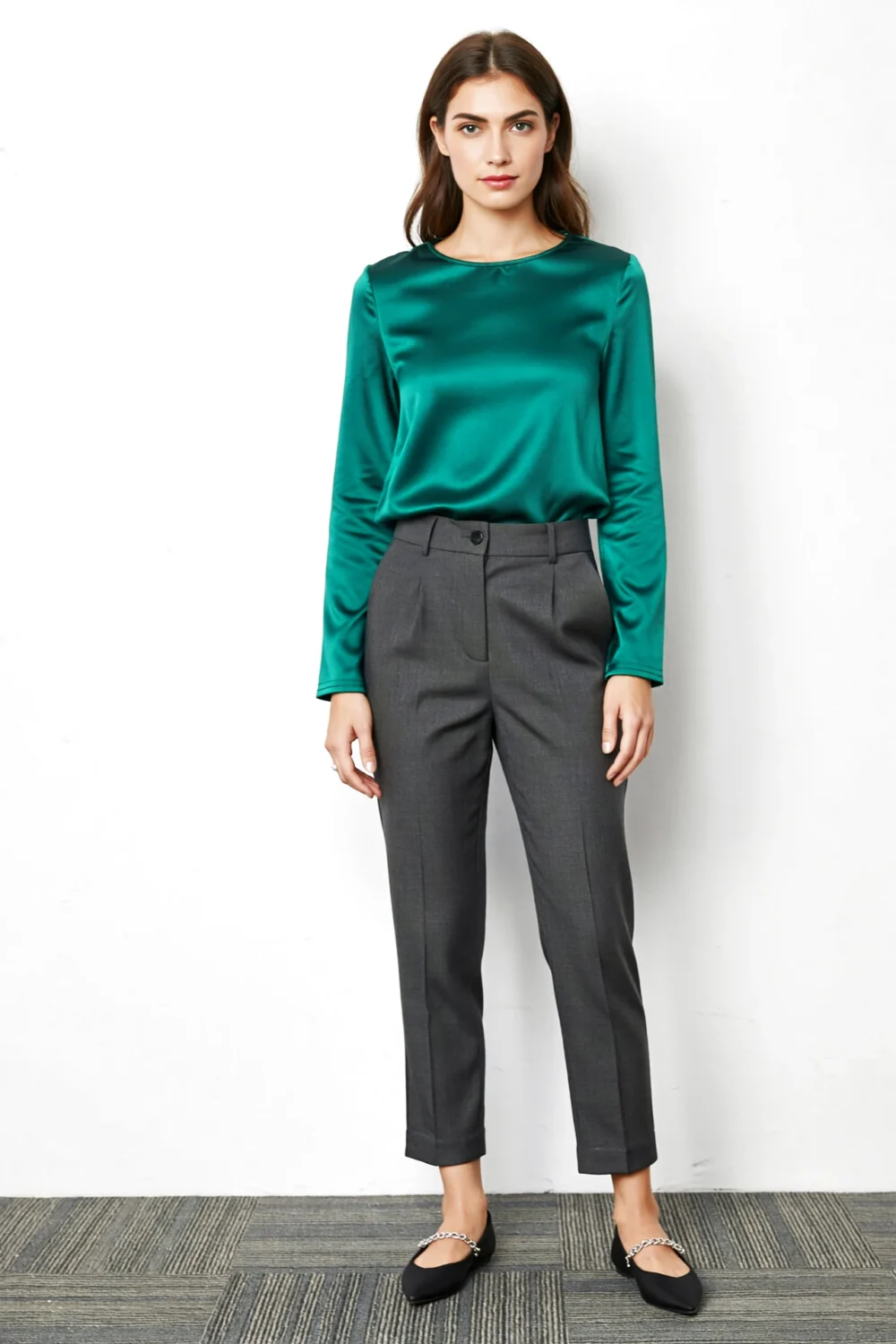 Woman in emerald satin top with charcoal trousers, silver chain flats, polished business-friendly outfit for workwear styling