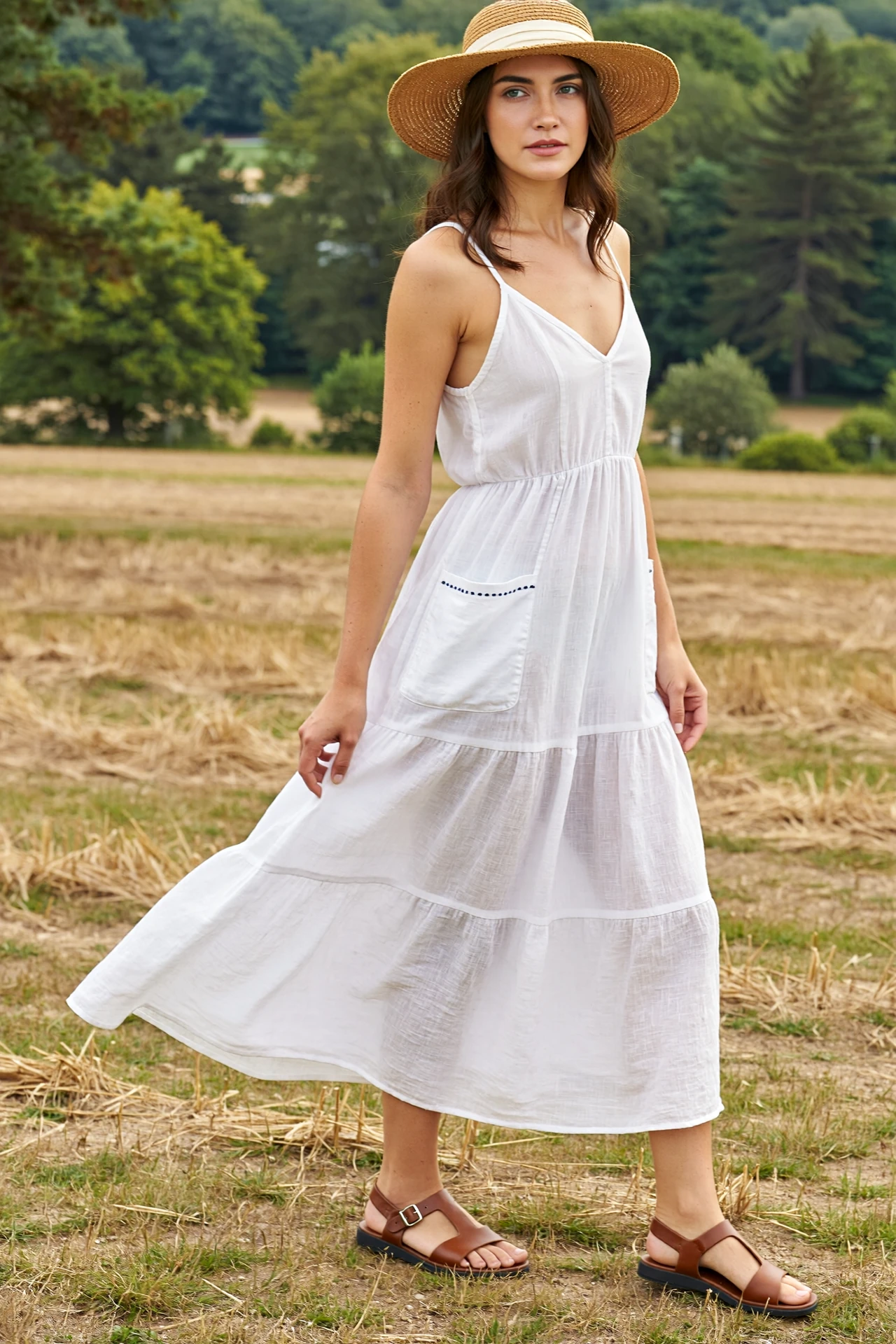 Woman in a white flowy sundress, flat strappy sandals, and wide-brim hat posing outdoors in a breezy summer concert outfit
