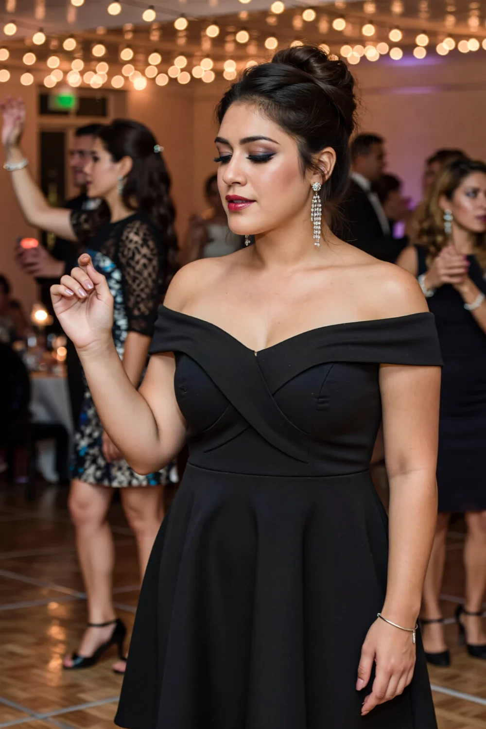 Woman with hair up wearing chandelier earrings in an off-shoulder black dress, simple bracelet, dancing under twinkling lights