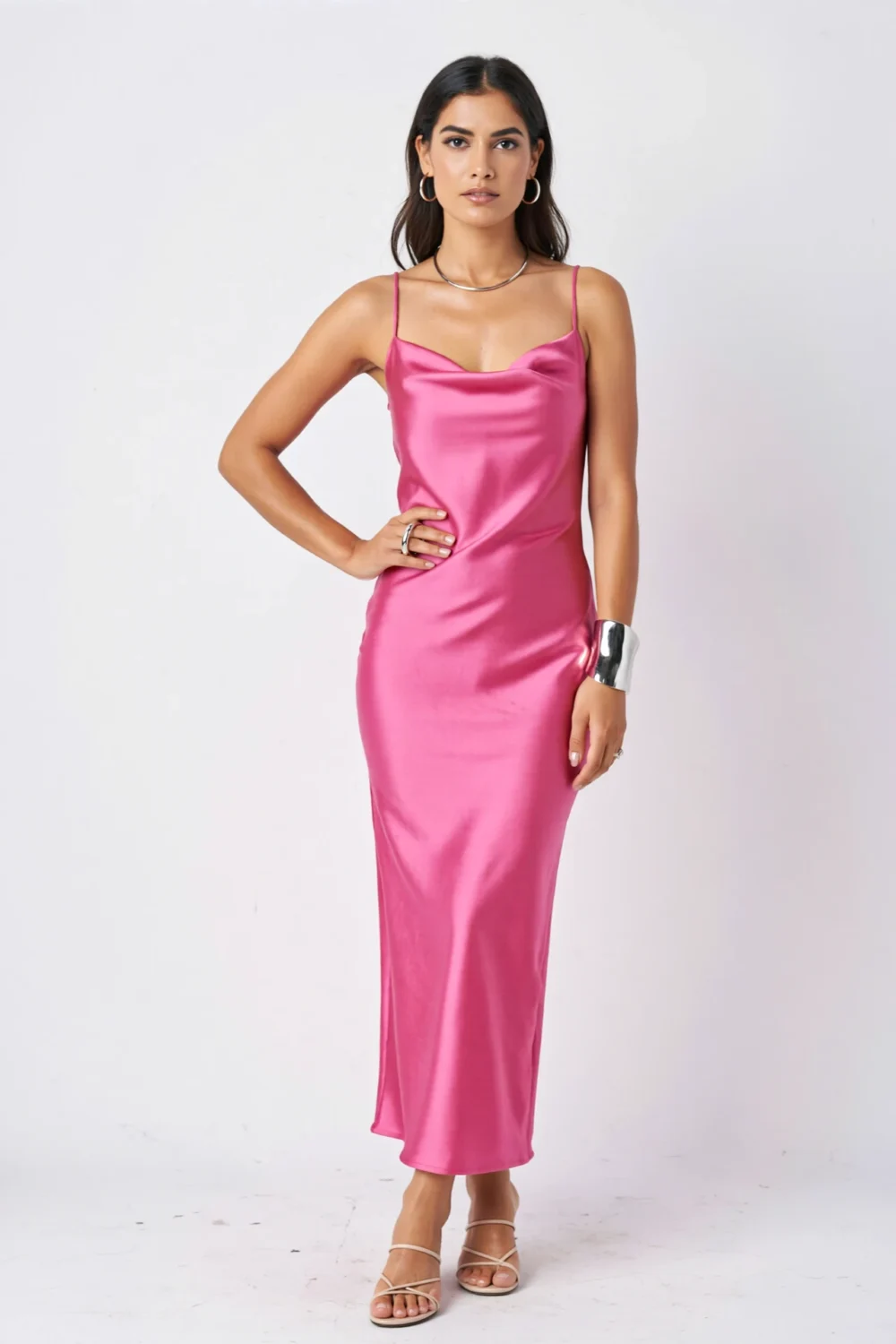 Model in a hot pink satin dress styled with minimal silver hoop earrings, sculptural cuff bracelet, and strappy nude sandals, fashion-forward look