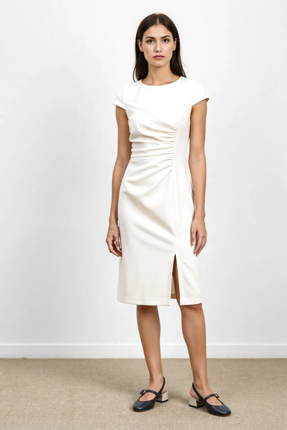 Model in a structured knee-length cream dress with side ruching and front slit, with low block-heel flats for a professional look