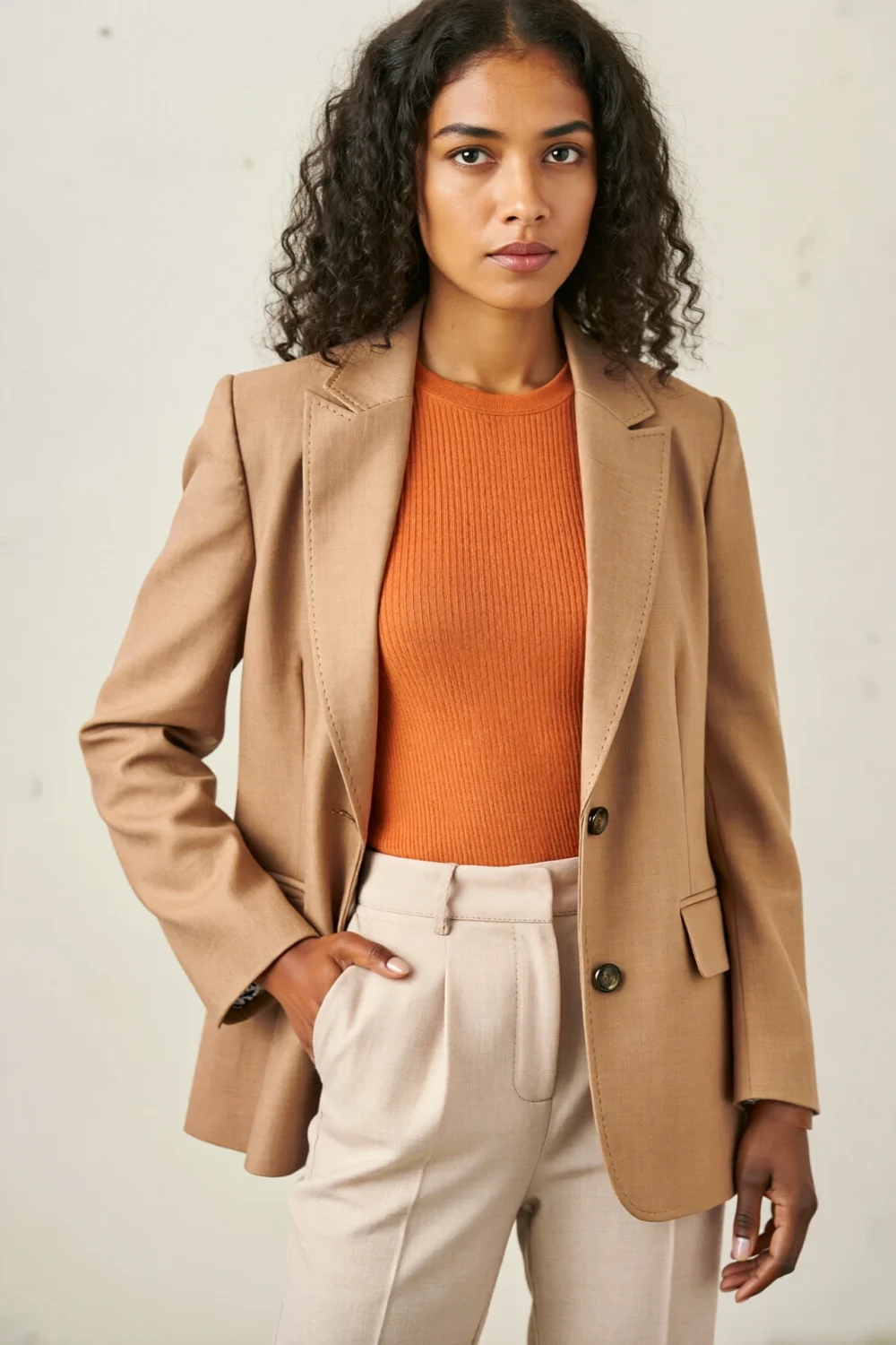 Woman in beige blazer and cream trousers, layered over a fitted orange ribbed top for a polished, modern contrast.