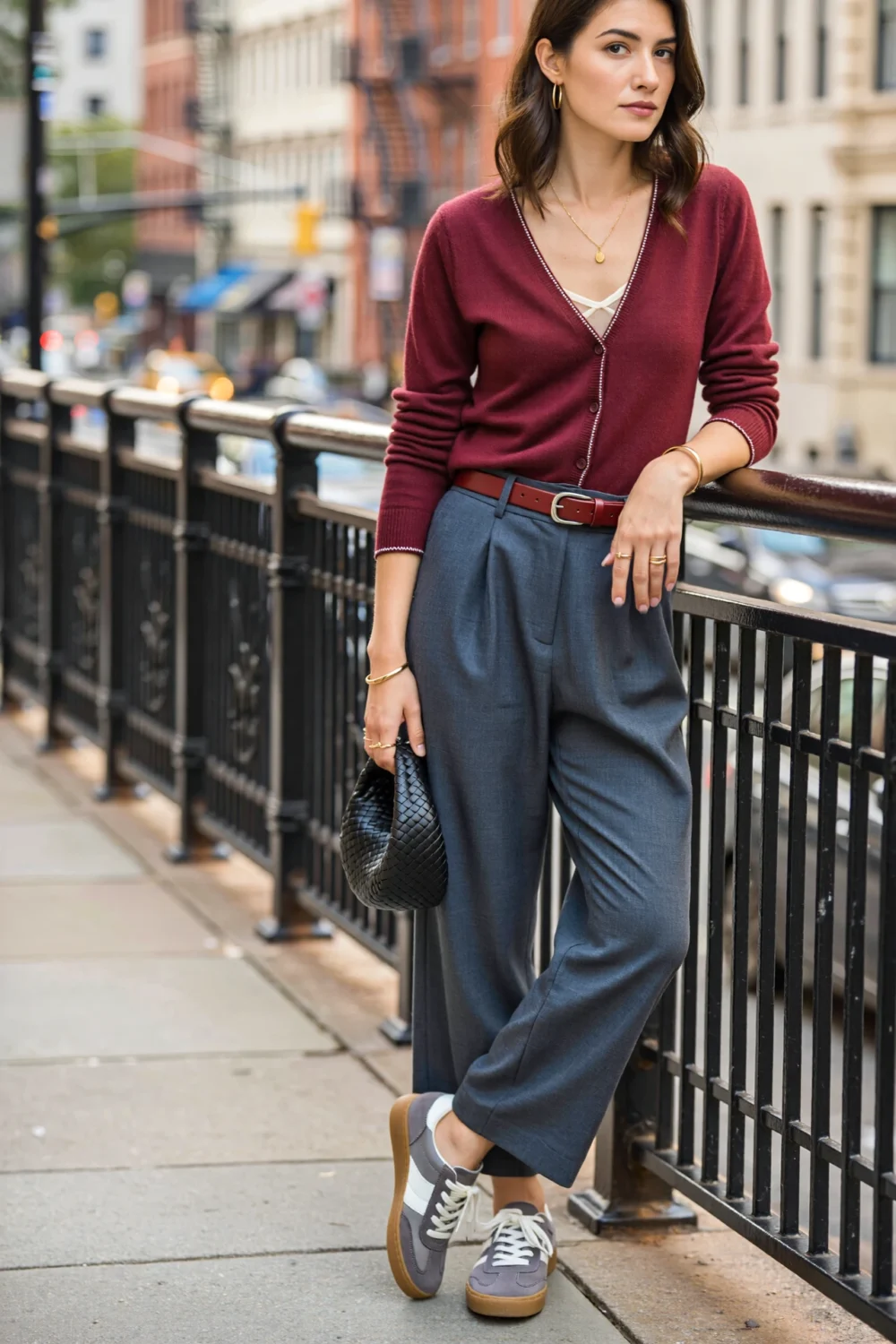 Woman in merlot cardigan and slate-gray trousers with retro sneakers, city-ready casual look on an urban sidewalk with black bag