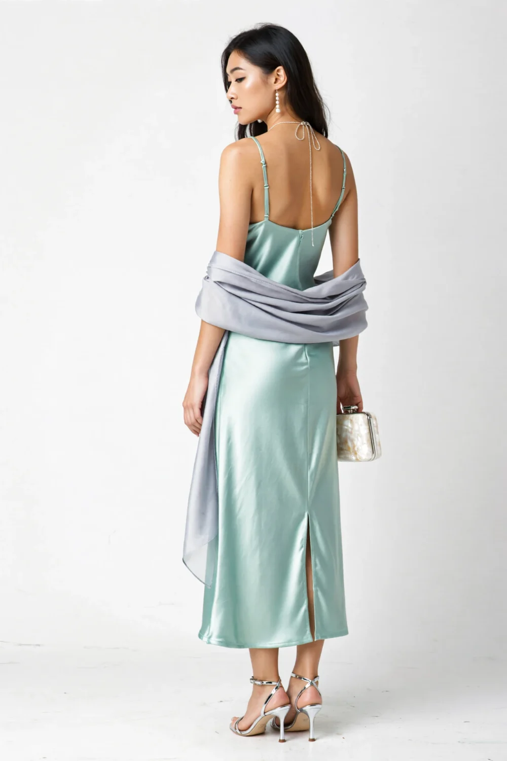 Mint satin cowl-back slip dress with tiny back slit, mirrored platinum sandals, and an oyster box clutch for a sleek modern look