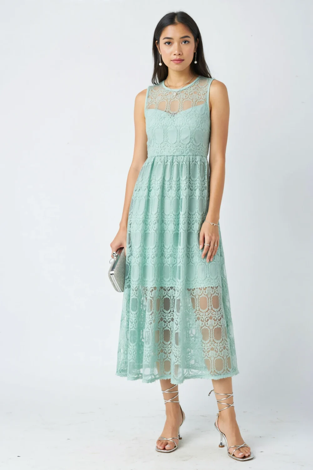 Model in mint green lace midi dress with silver minimalist strappy sandals, holding a silver clutch against a clean white backdrop.