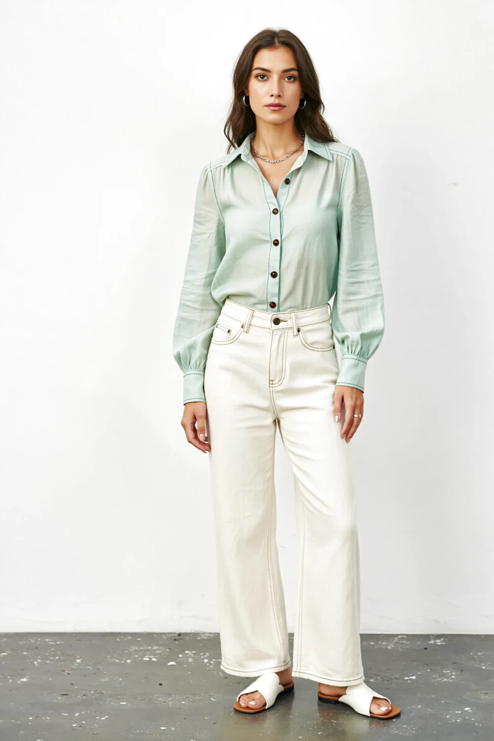 Woman in mint blouse with wide-leg cream jeans, silver chain, and white slides, creating a fresh, leg-lengthening look