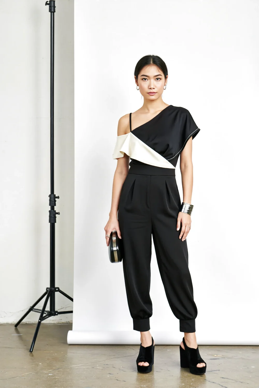 Model in a tailored black crepe monochrome jumpsuit with ivory diagonal panel, asymmetric one-shoulder cut and tapered ankle legs