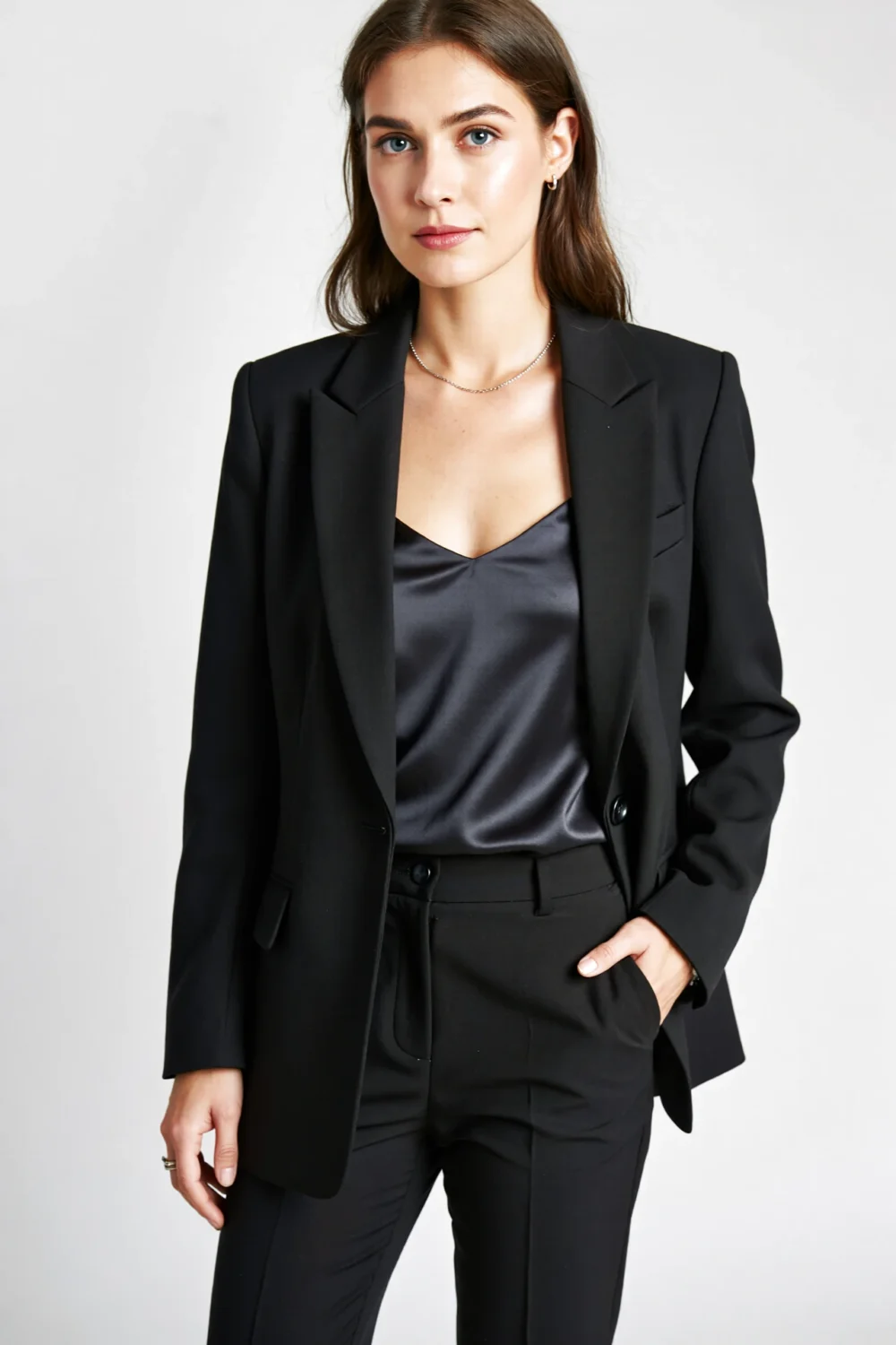 Woman in black monochrome suit with slim trousers and single-button blazer, wearing a satin camisole and minimal jewelry, modern.