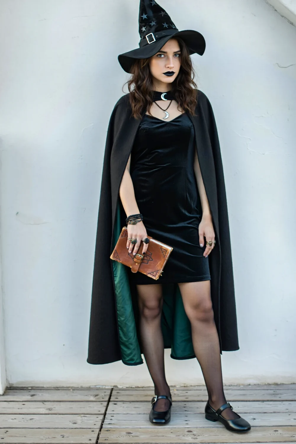 Moonlit spellcaster in velvet mini, cape, starry hat, and black tights, styled with moon pendant and cognac clutch for a chic witchy look