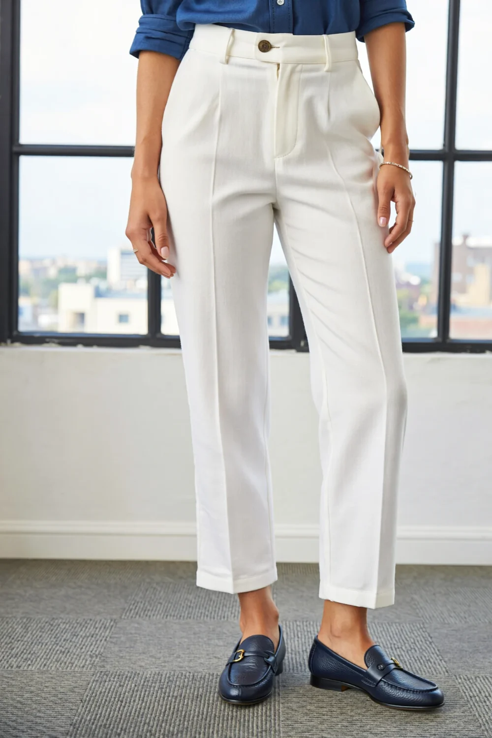 Navy loafers with brass hardware, paired with bright white tailored trousers and a blue shirt for a polished nautical look