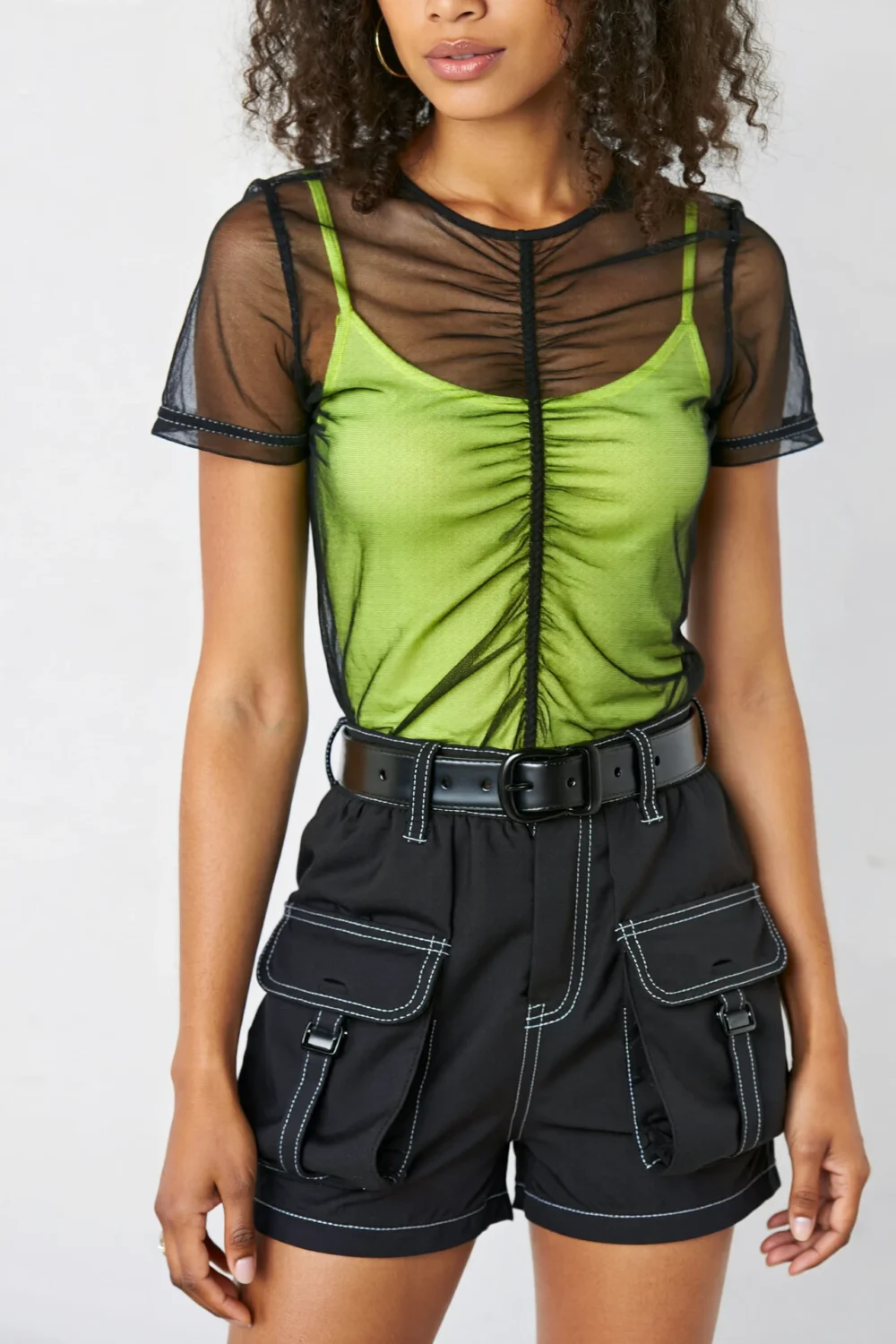 Neon green bodysuit with sheer black overlay and black cargo mini shorts, creating a bold futuristic streetwear contrast style