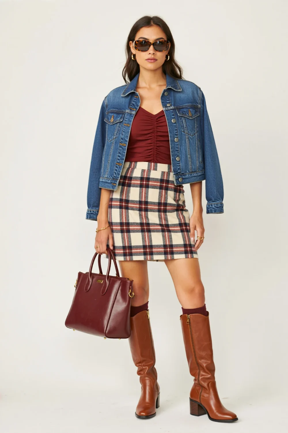 Fashion model in oxblood top, plaid mini skirt, denim jacket, chestnut knee-high boots, and burgundy tote for a chic weekender look