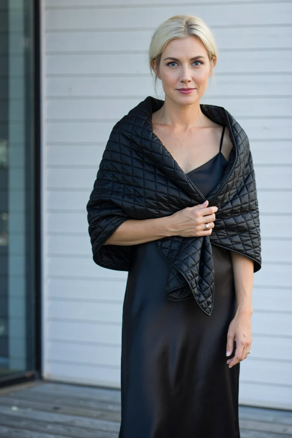 Woman in a black slip dress wearing a black quilted padded stole draped over shoulders, a sleek dress-friendly slim puffer warmth