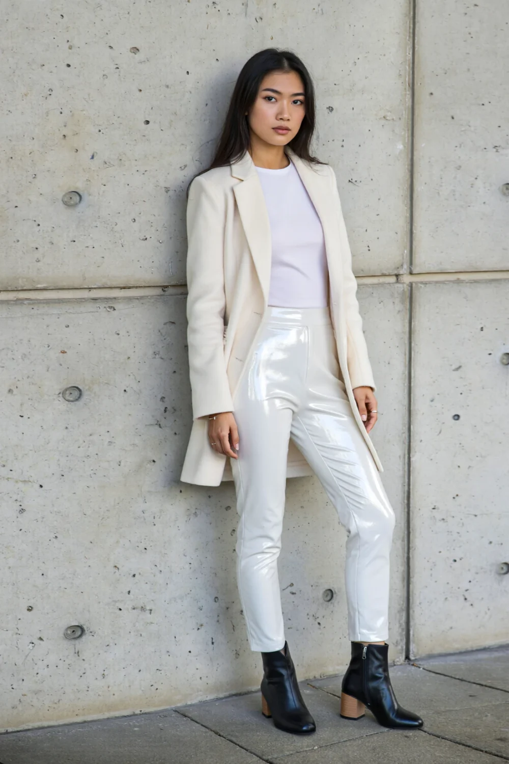 Woman in cream blazer and glossy white pants paired with black matte ankle boots, creating a sleek, modern contrast against concrete.

