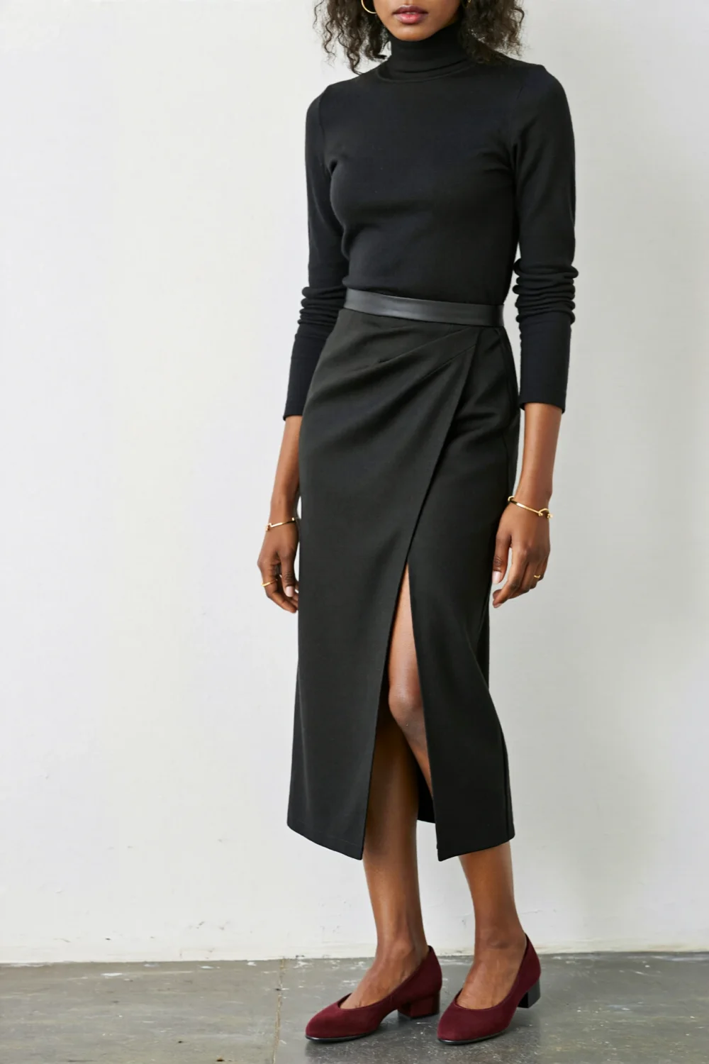 Minimal black merino turtleneck and bias-cut skirt styled with deep burgundy pumps for a sleek, understated office look