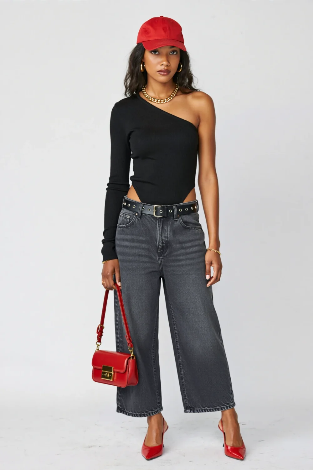 Fashion model in a black one-shoulder bodysuit with charcoal jeans, red cap, bag, and heels for a bold concert-ready night-out look