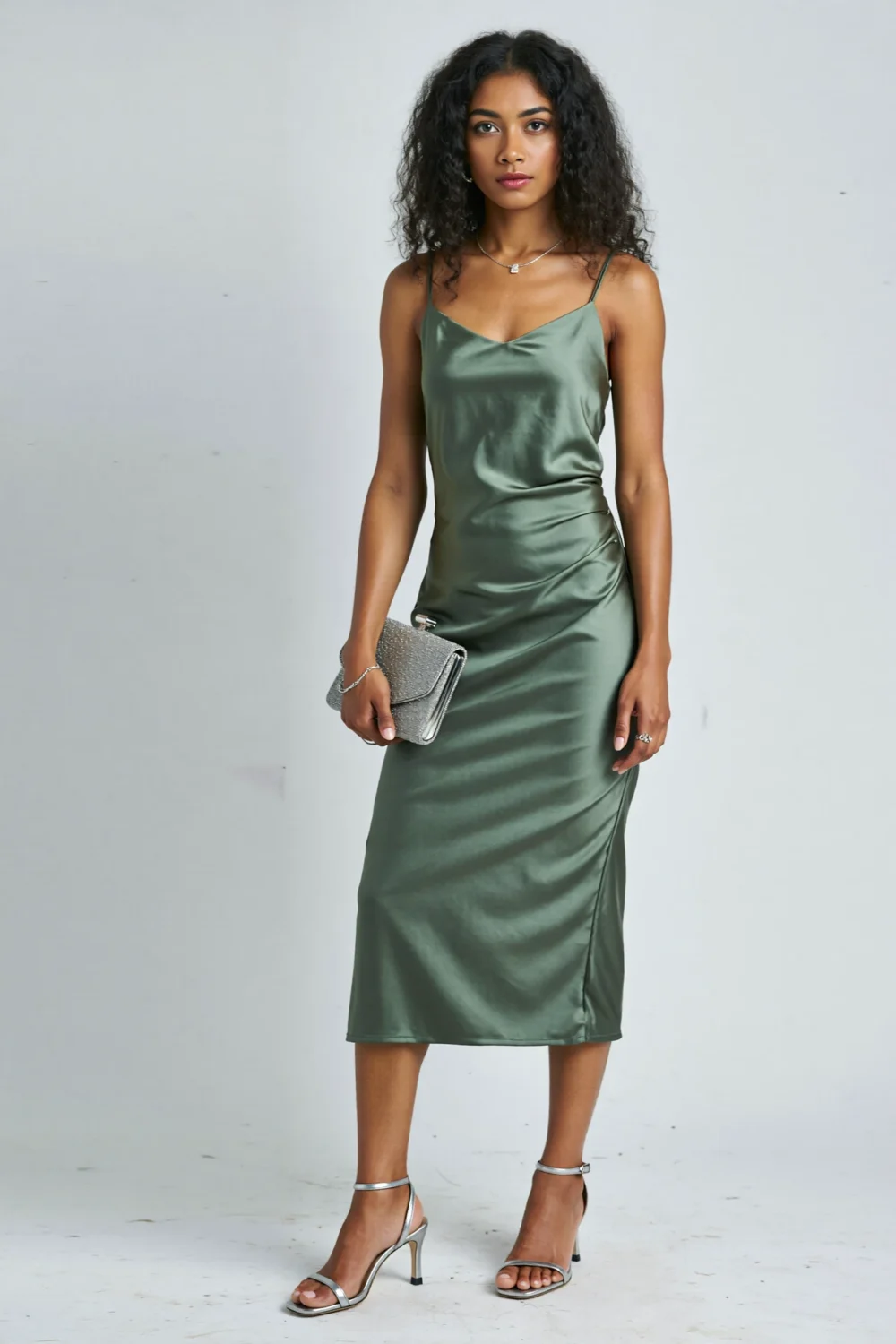 Woman in a sage green satin midi dress styled with brushed pewter soft silver heels and clutch for a chic, modern evening look