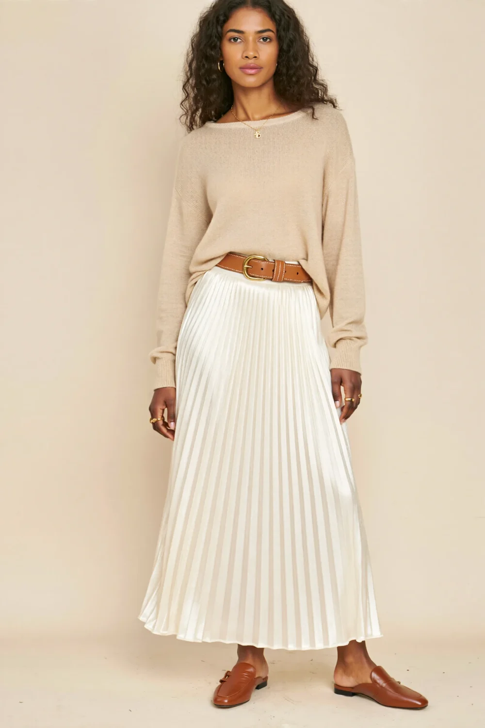 Model in beige knit sweater, white pleated maxi skirt, camel belt, and brown mules for a soft tonal sand-inspired outfit