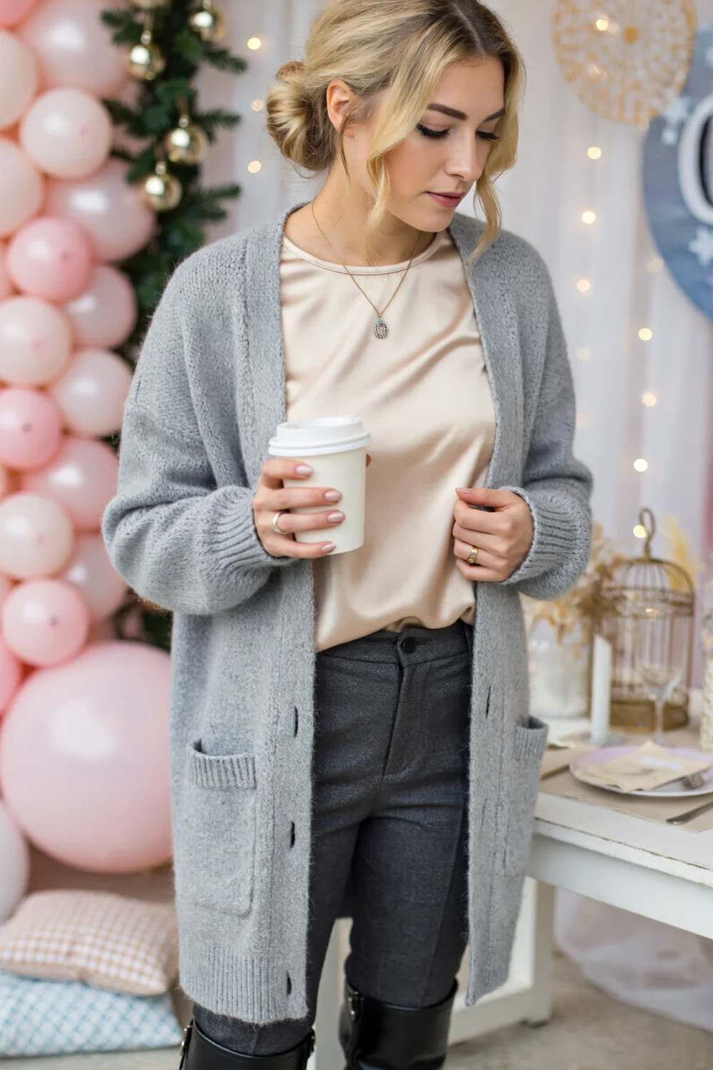 Woman wearing a satin blouse layered under a cozy grey cardigan, tucked into tailored trousers with ankle boots and a necklace