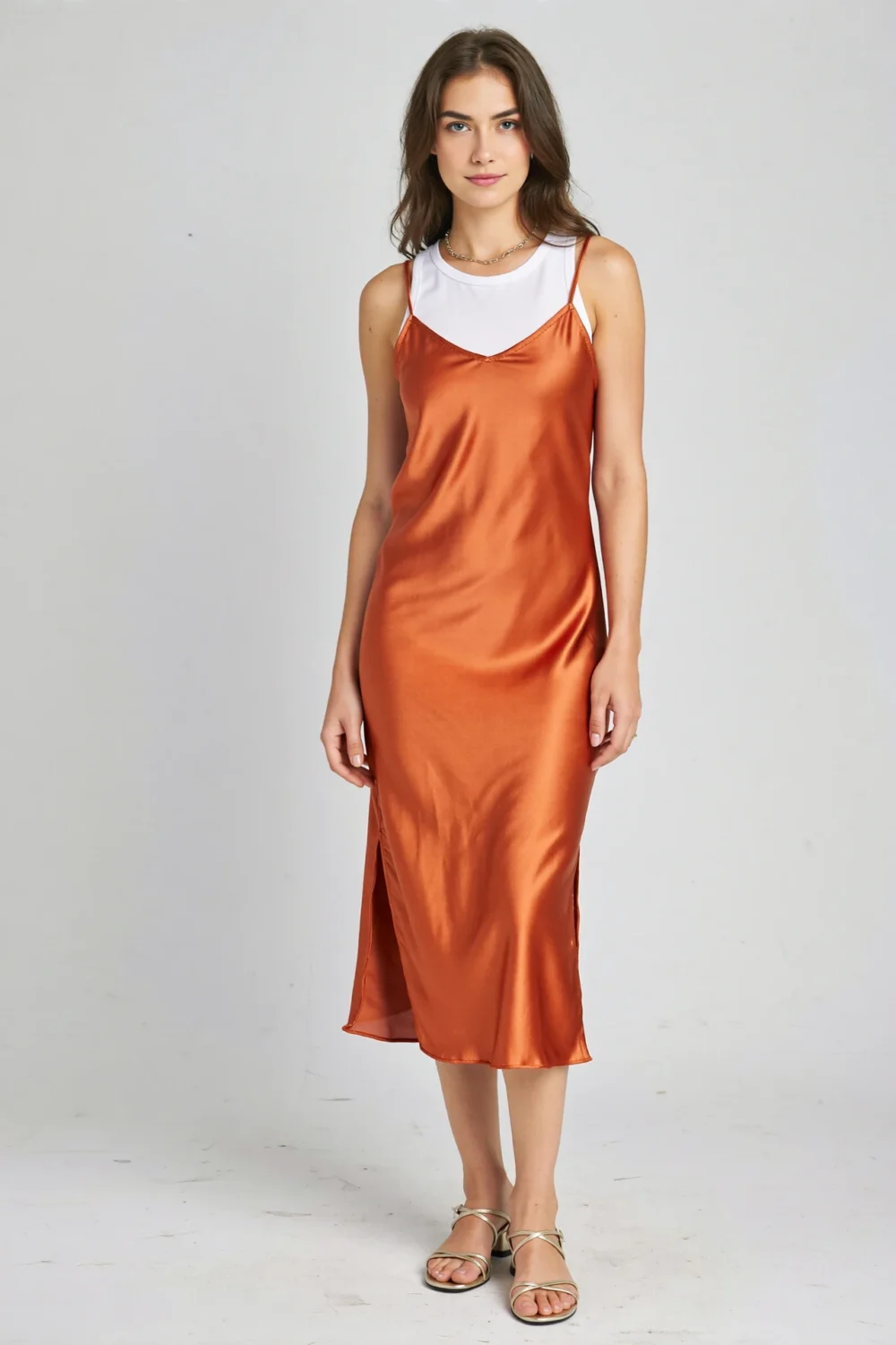 Orange satin slip midi dress layered over a white tank, styled with strappy sandals and a delicate chain necklace for a modern look