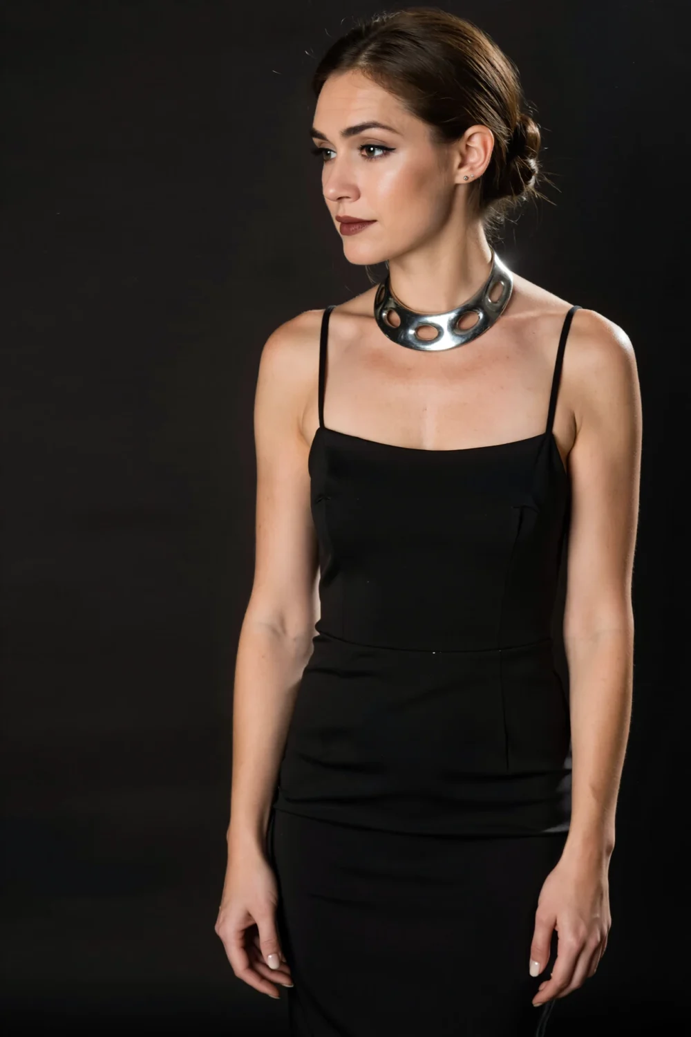 Model in a black dress wearing a bold sculptural silver collar with circular cutouts, a fashion-forward, evening-ready statement.
