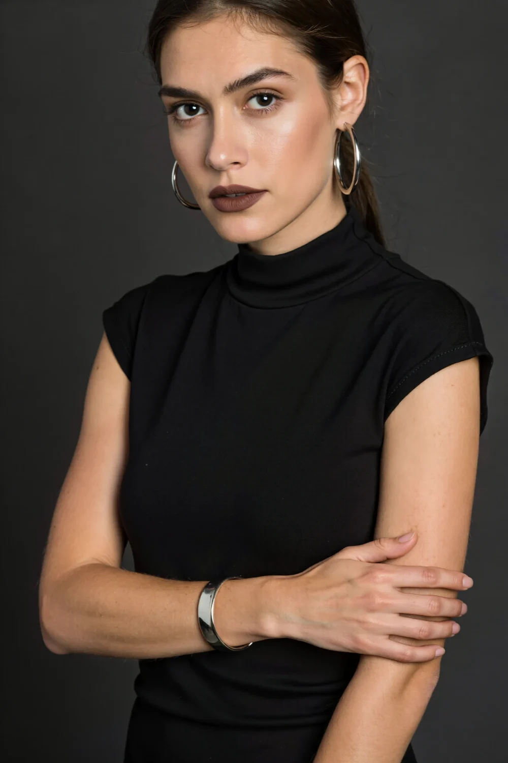 Model in high-neck black LBD wearing sculptural silver hoops and a knife-edge bangle, editorial modern look from gallery to dinner