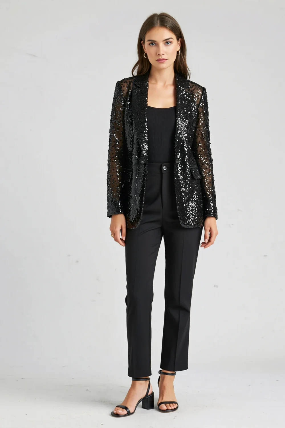 Woman in a black sequin blazer, matte black tank and tailored trousers, creating a sleek balanced evening look with subtle sparkle