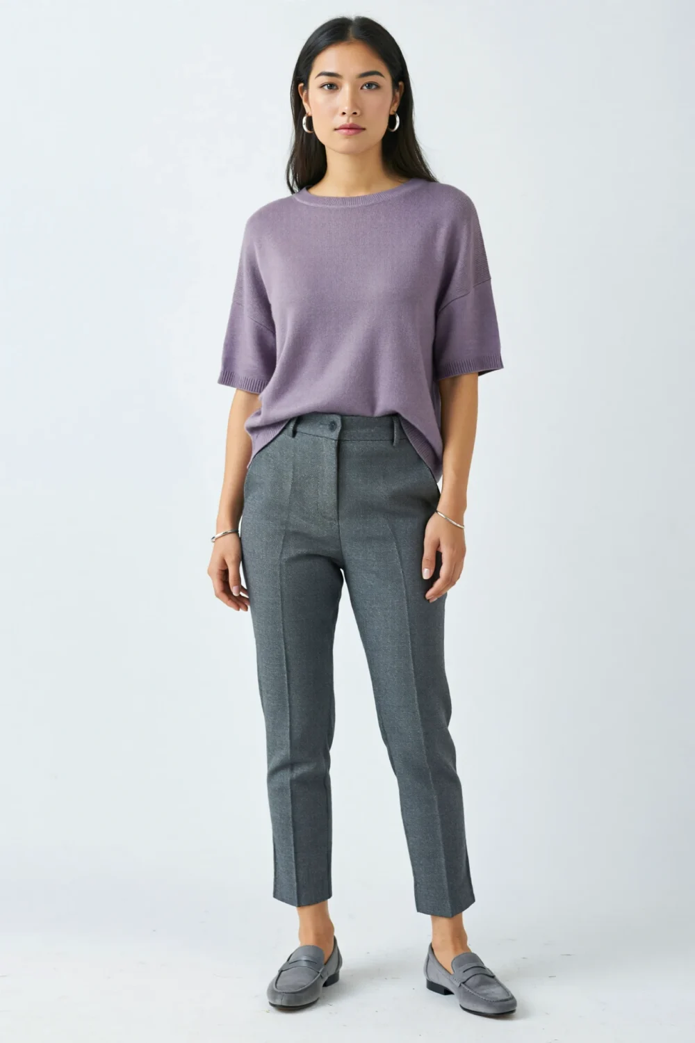 Woman in lavender knit tee, slate grey ankle trousers, silver hoops, and grey suede loafers for a polished, airy look