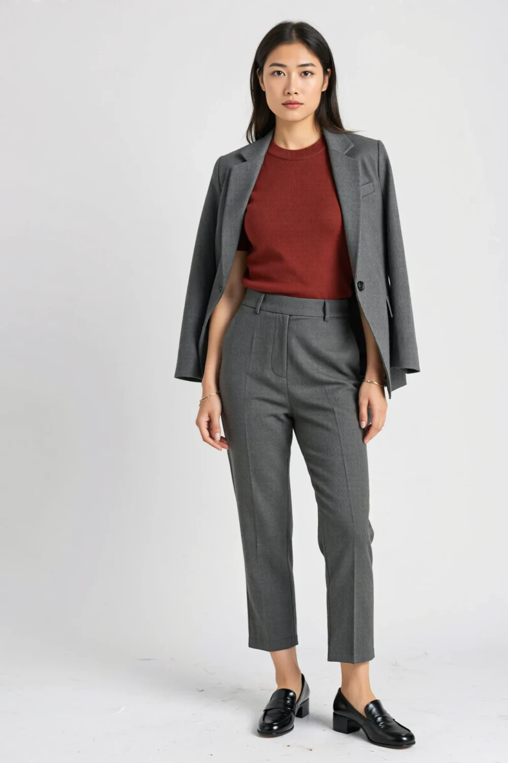 Woman in slim grey ankle pants, burgundy sweater shell, and tonal grey blazer with black loafers for a modern office-ready look.