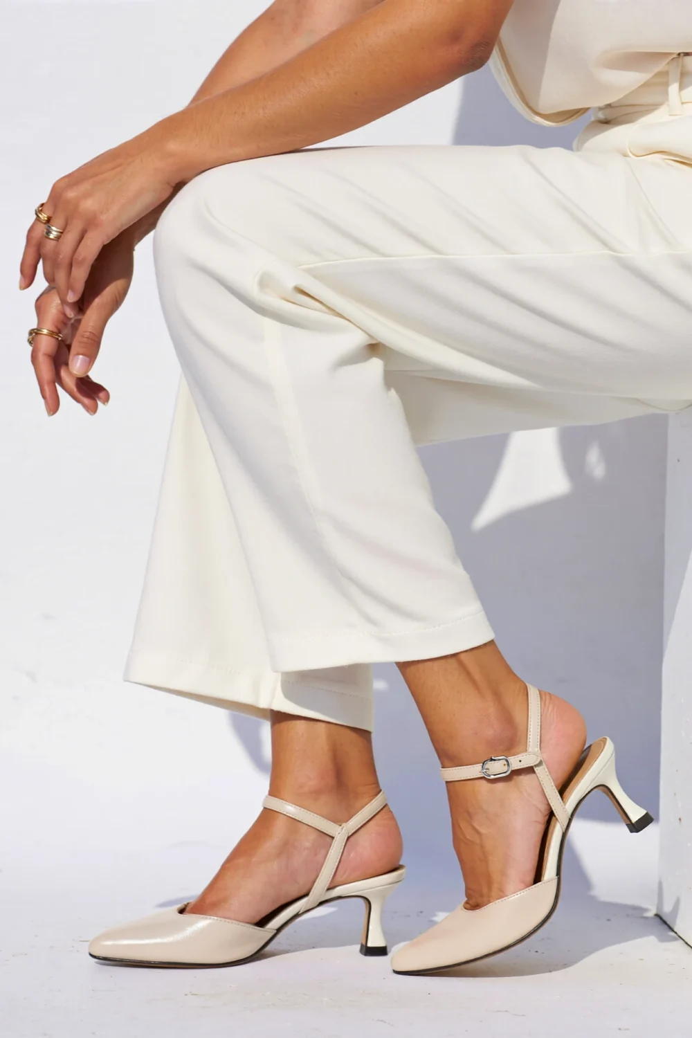 Cropped white pants styled with beige slingback heels, showing pointed toes and ankle straps for a sleek, elegant finish
