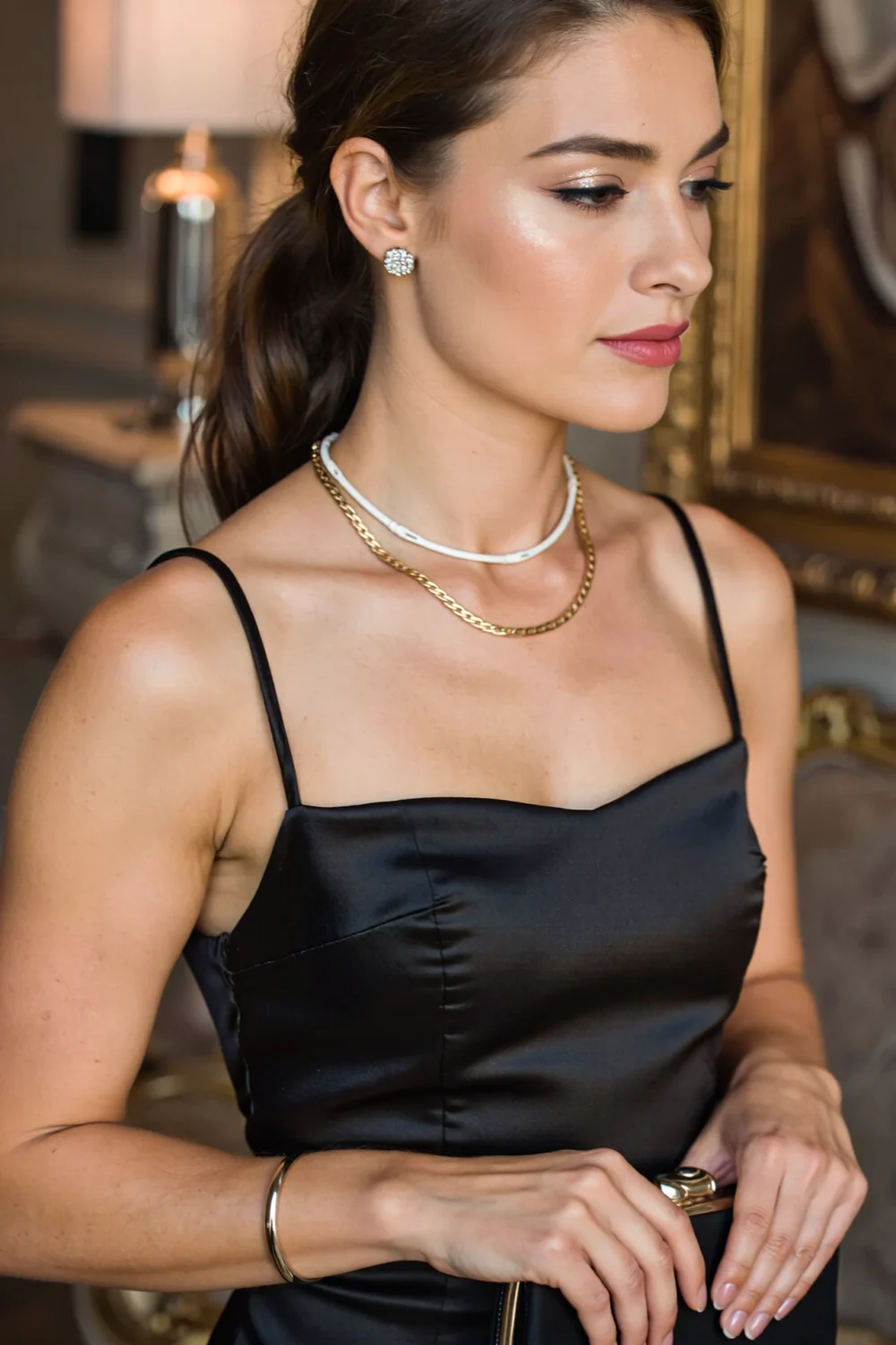 Model in a little black dress wearing a slim tennis necklace layered over a flat herringbone chain, pavé studs and slim bangle.