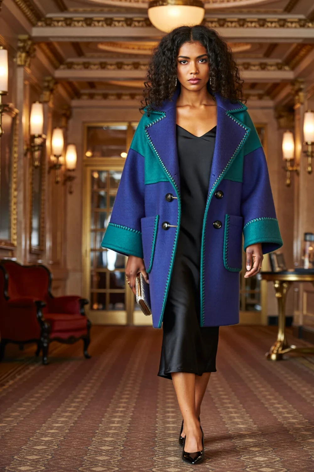 Model in jewel-toned cocoon coat over sleek black dress, carrying metallic clutch, styled for an elegant dramatic entrance