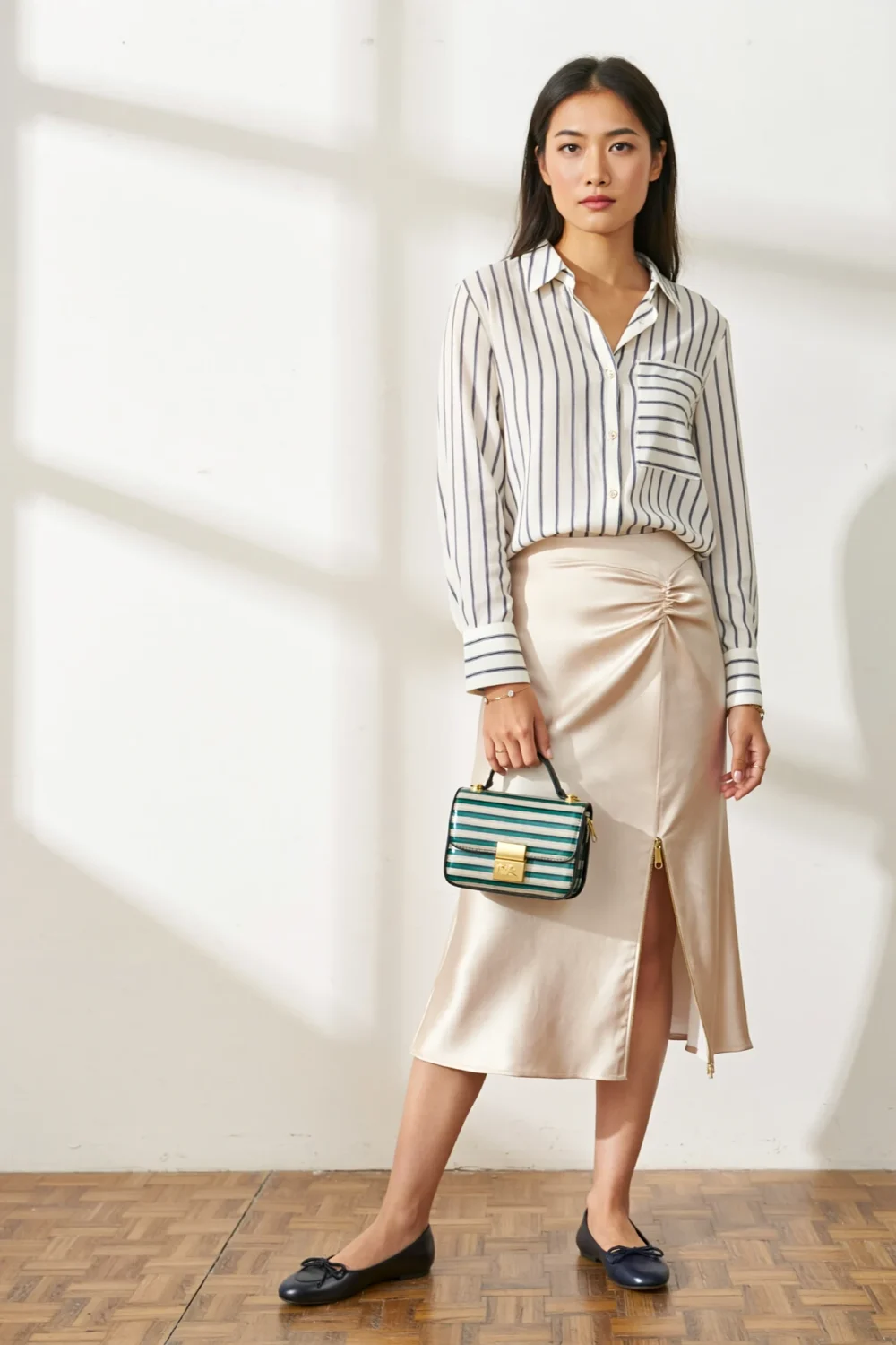 Woman in striped button-up, satin midi skirt and ballet flats, carrying a striped compact bag for a polished, elevated look